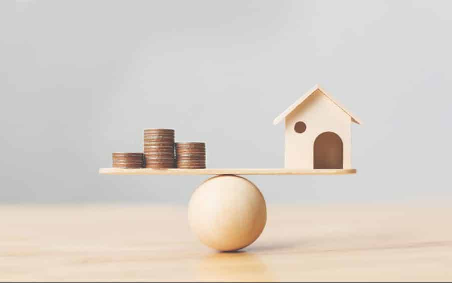 Wooden home and money coins stack on wood scale. Property investment and house mortgage financial real estate concept