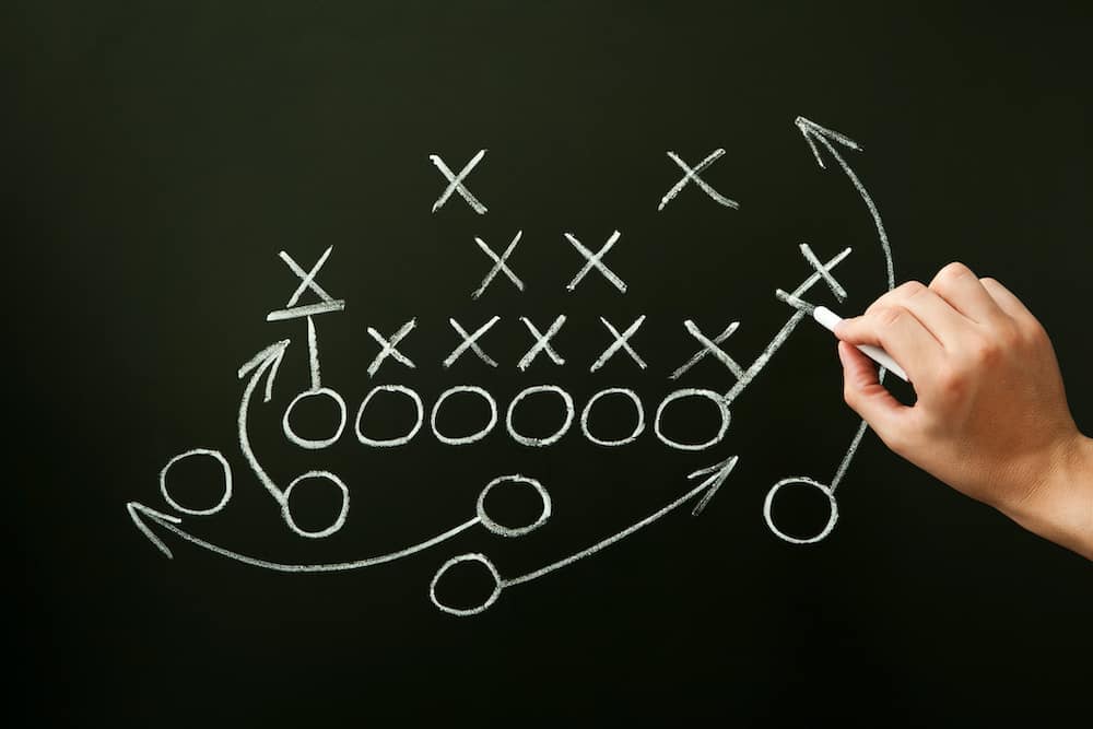 Coach drawing american football or rugby game playbook, strategy and tactics with chalk on blackboard.